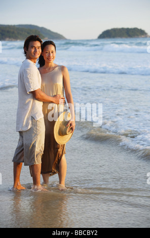 Couple standing on beach, ankle deep in water, looking at camera Stock Photo