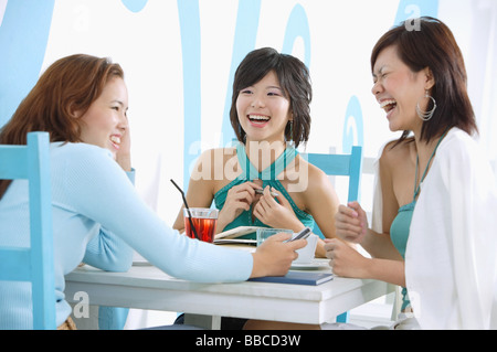 Three young women sitting in cafe, laughing Stock Photo
