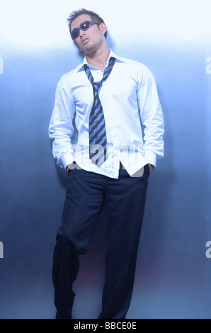 Man wearing shirt, tie and sunglasses, leaning on wall Stock Photo