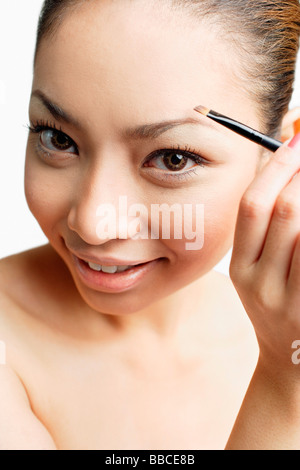 Young woman using eyebrow brush, looking at camera Stock Photo