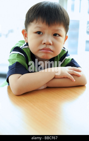 Young boy looking away, arms crossed, leaning on table Stock Photo