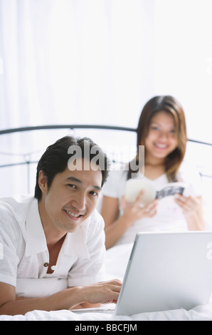 Couple in bedroom, man using laptop, smiling at camera Stock Photo