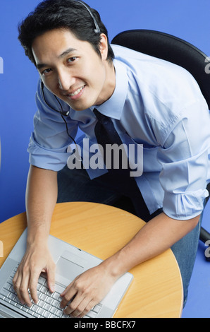 Man wearing headset, using laptop, smiling up at camera Stock Photo