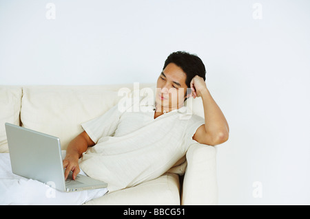 Man lying on sofa, using laptop Stock Photo
