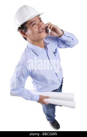 Mature man wearing construction hat, using mobile phone, carrying blueprints Stock Photo
