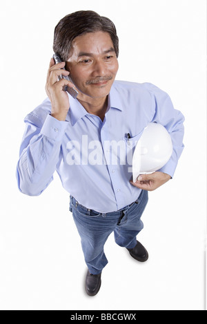 Mature man holding construction hat, using mobile phone Stock Photo