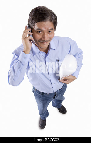 Mature man holding construction hat, using mobile phone, looking at camera Stock Photo