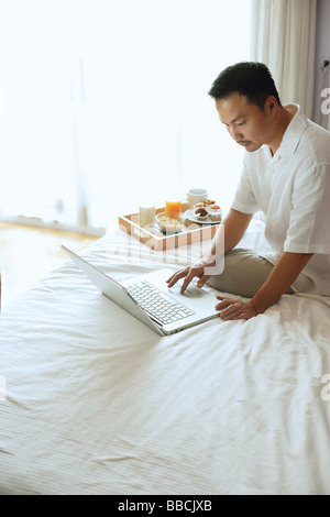Man sitting on bed, using laptop Stock Photo