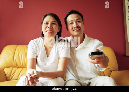 Couple sitting on sofa, watching TV, man holding TV remote control Stock Photo