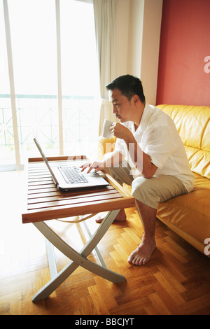 Man using laptop, drinking from mug Stock Photo