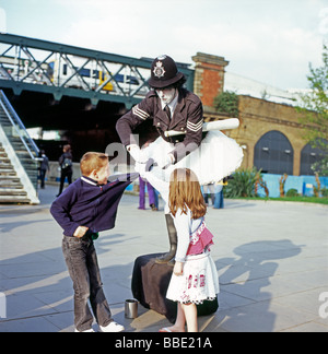 A street entertainer dressed as a London policeman London bobby ties the sleeves of two kids children together on the Southbank, London England UK Stock Photo