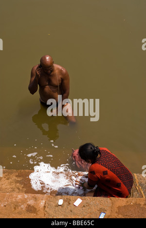 Traditional Indian couple, man talking on his cell phone, woman washing clothes. Stock Photo