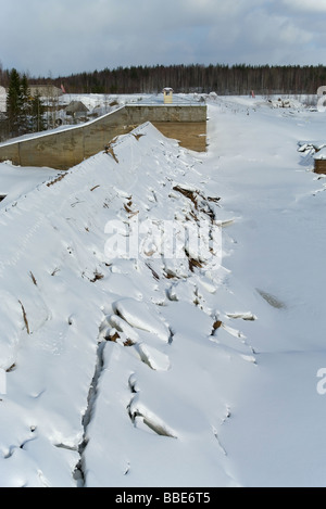 Water overflow on the man-made reservoir storage in winter season. It is in the forest. White snow and cracked ice. Stock Photo
