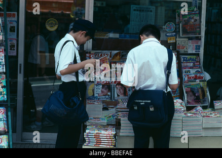 JAPAN Chiba Narita Two Junior High Japanese schoolboys in uniform reading magazines from pavement sidewalk stand Stock Photo