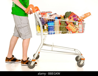 Unidentified male, wear shorts and sneakers pushing supermarket shopping trolley filled with weekly shopping on white background Stock Photo