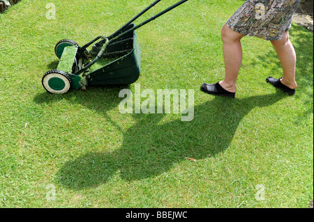 Female mowing the lawn casting a shadow over the grass in sunshine Stock Photo