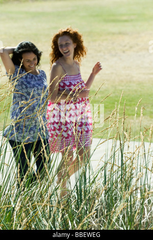 Two young women walking arm in arm outdoors, both laughing Stock Photo