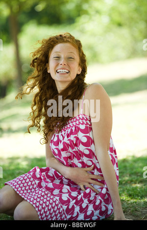 Young red haired woman sitting outdoors, laughing, portrait Stock Photo