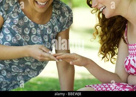 Two women sitting outdoors, looking at one woman's hand, both smiling Stock Photo