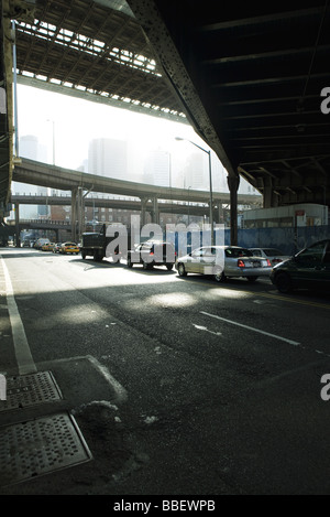 Traffic waiting at traffic signal on street beneath elevated road Stock Photo