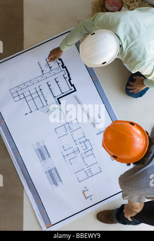 Two men crouching looking over blueprints spread out on floor Stock Photo