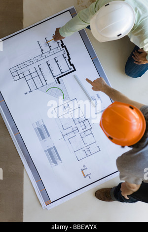 Two men crouching discussing blueprints spread out on floor Stock Photo