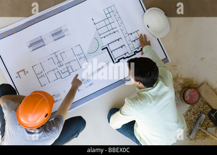 Two men reviewing blueprint spread out on floor Stock Photo