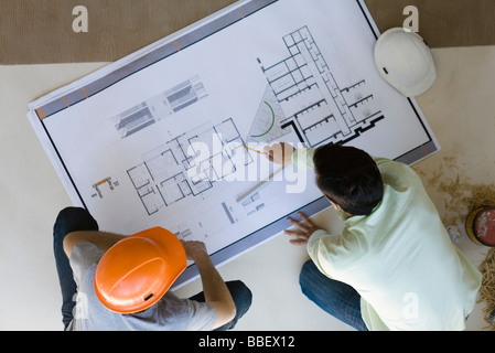 Two men side by side reviewing blueprint spread out on floor Stock Photo