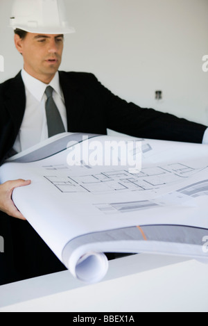 Man in suit and hard hat unrolling blueprint Stock Photo