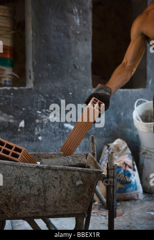 Construction worker placing brick in wheelbarrow Stock Photo