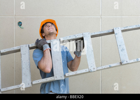 Construction worker carrying ladder, looking up Stock Photo