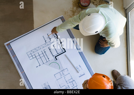 Two men reviewing blueprint spread out on floor Stock Photo