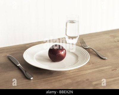 Place setting with a plate, a single apple, knife, fork and a glass of water Stock Photo