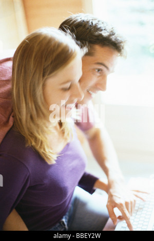 Couple typing on keyboard together, man leaning over woman's shoulder Stock Photo