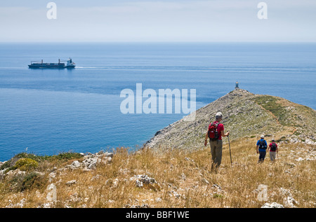 Walkers on a ridge descending to the Lighthouse at the tip of Cape Tenaro in the deep Mani Peloponnese Greece Stock Photo