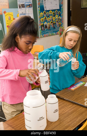 Two school children 8-9 year old working together pour fluid multi ethnic racial  racially diverse multicultural cultural interracial POV United States Stock Photo