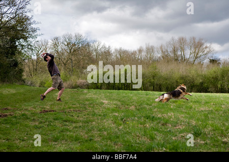 Man throwing a red rubber ring toy for German Shepherd dog in grassy field in Bristol with dog racing after it Stock Photo