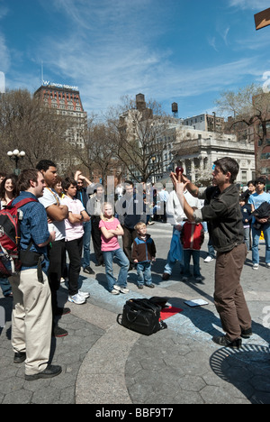 a crowd of young adults & children gather to watch a young man performing sleight of hand in Union Square park, New York City Stock Photo
