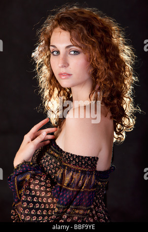Portrait of an attractive young woman with curly hair posing on black with hair light Stock Photo