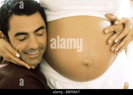 Man embracing pregnant wife, resting his cheek on her stomach, cropped Stock Photo