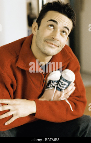 Man holding baby shoes, looking up and smiling Stock Photo