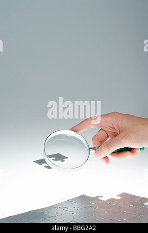 Person magnifying jigsaw piece Stock Photo