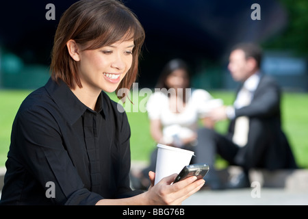 A beautiful young Eurasian woman with a wonderful smile texting on her cell phone while drinking coffee Stock Photo