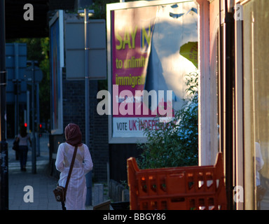 Young Muslim woman walks past a UKIP billboard reading 'say no to unlimited immigration'. Stock Photo