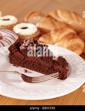 Chocolate Cake on a white plate with fork. Bread and other cakes in the background. On wooden table top. Studio setup. Stock Photo