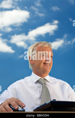 Business concept shot showing an older male executive using a computer with a blue sky complete with fluffy white clouds Stock Photo