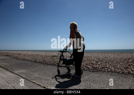 Elderly woman walking away from camera alongside the beach into the sunset Stock Photo
