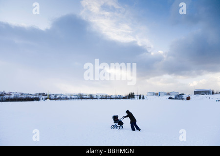 A woman walking with a pram in the snow. Hafnarfjordur, Greater Reykjavik Area, Iceland Stock Photo