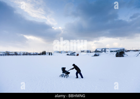 A woman walking with a pram in the snow. Hafnarfjordur, Greater Reykjavik Area, Iceland Stock Photo