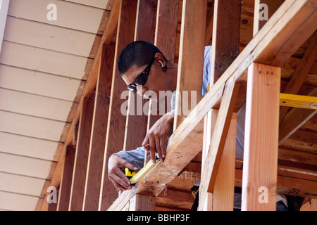Mexican American carpenter using a measuring tape while doing rough framing on a residential remodel construction job Stock Photo